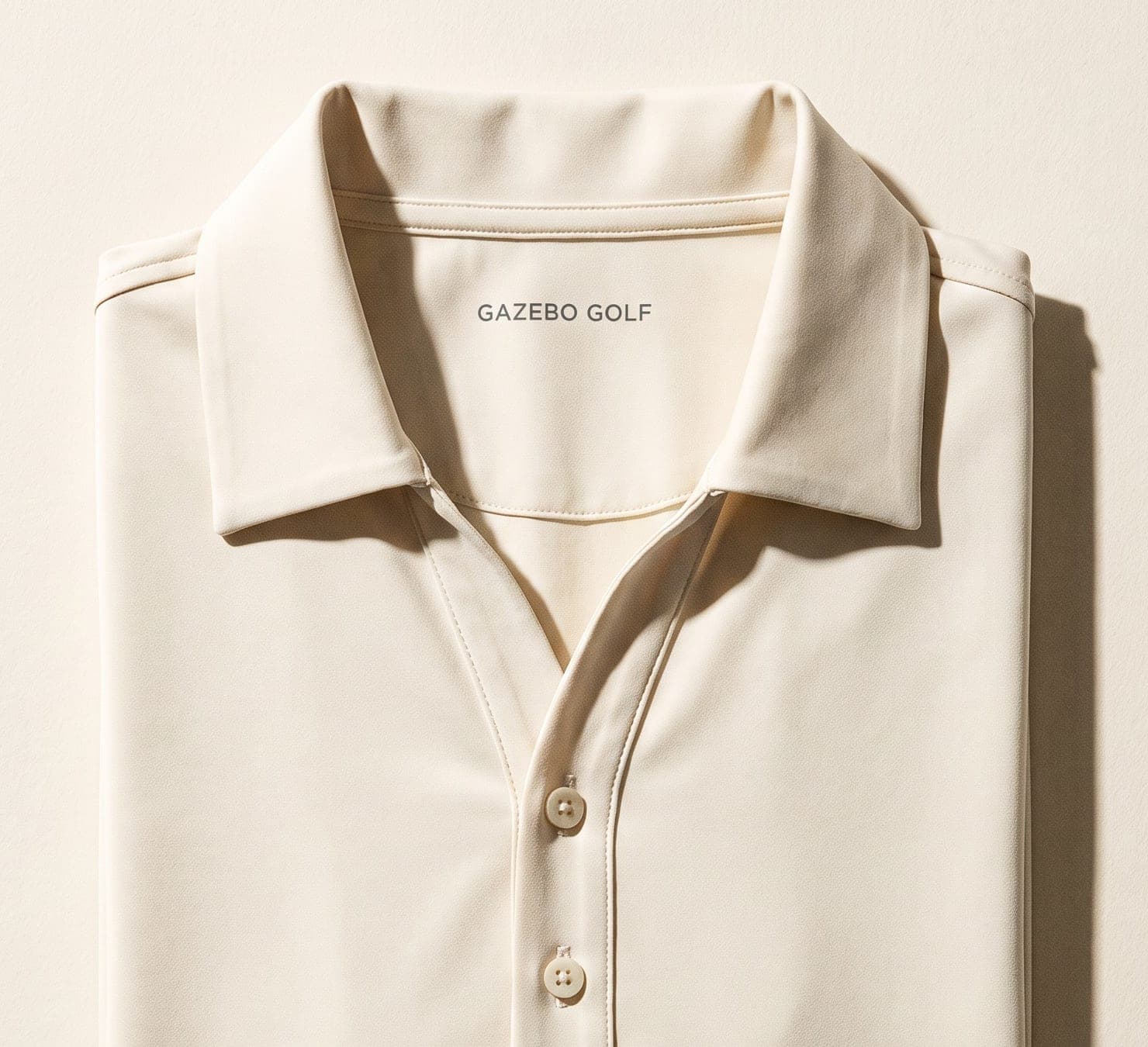 A folded cream performance golf polo in technical stretch jersey seen from above, its two-button placket and folded collar visible, with GAZEBO GOLF printed in small charcoal letters on the inner back neck.